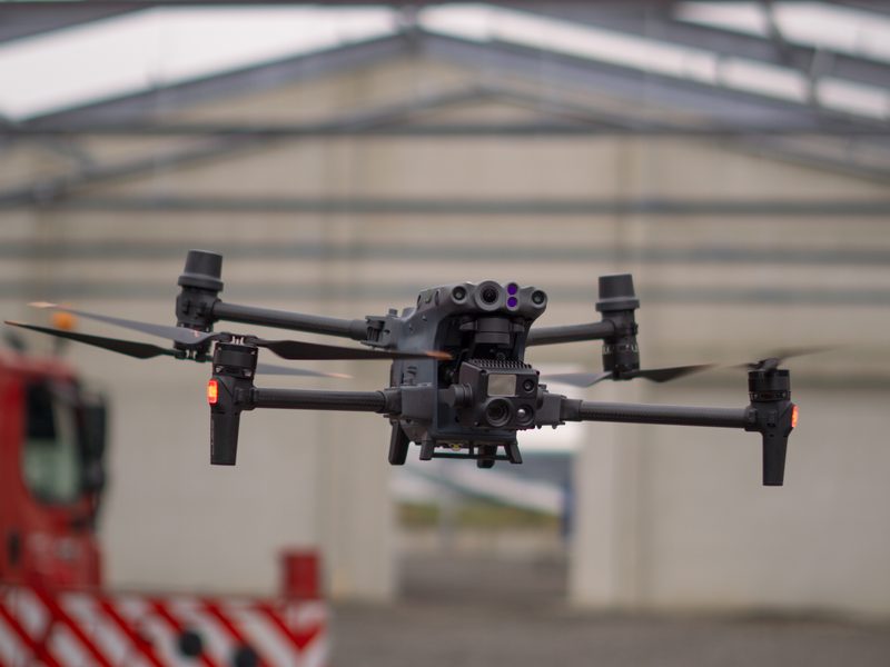 Eigene Inspektionsdrohne im Schwebeflug vor einer Industriehalle, Sensorkopf mit Kameramodulen erkennbar
