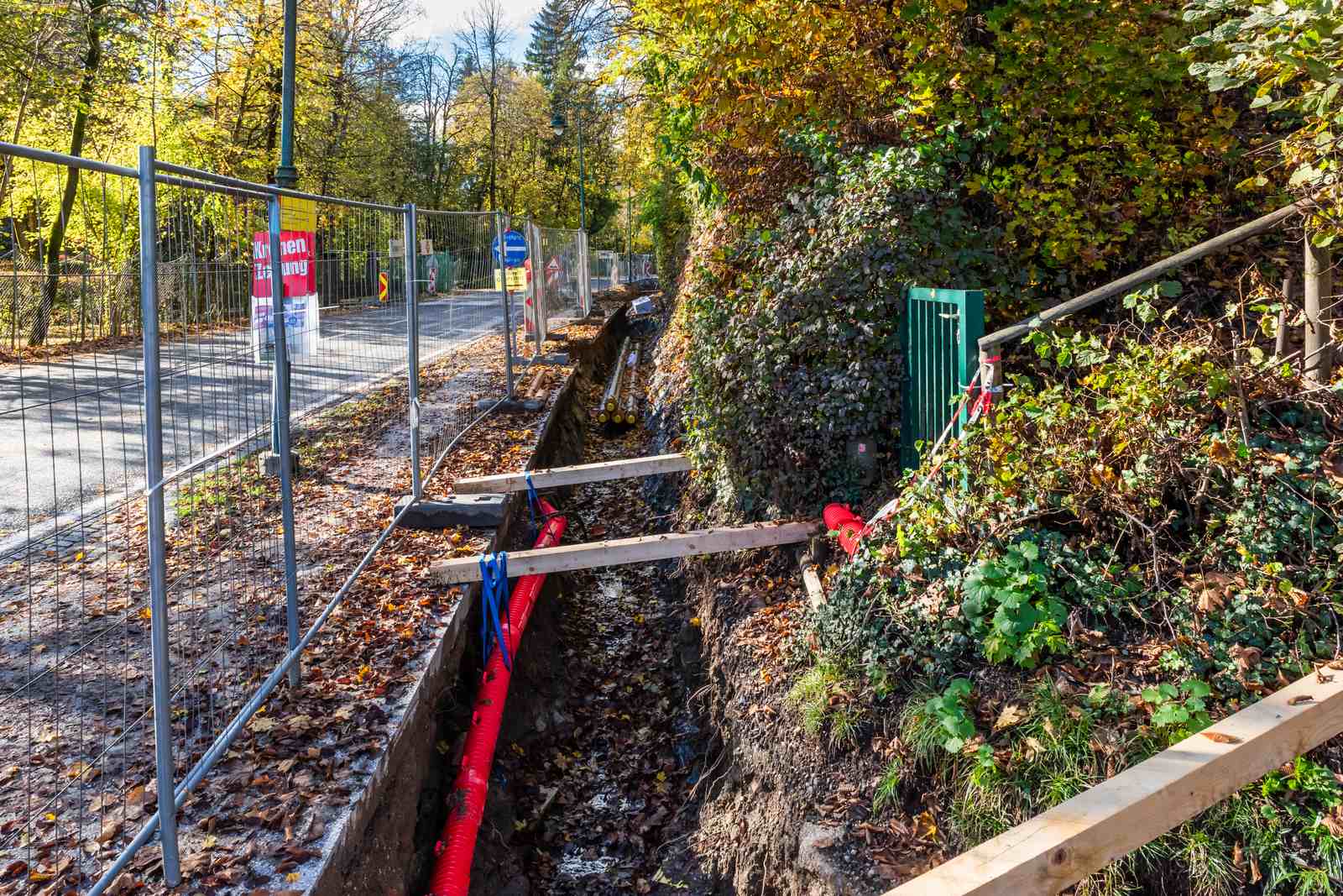 Offener Leitungsgraben mit Fernwärmerohr bei Tiefbauarbeiten im Herbstlaub